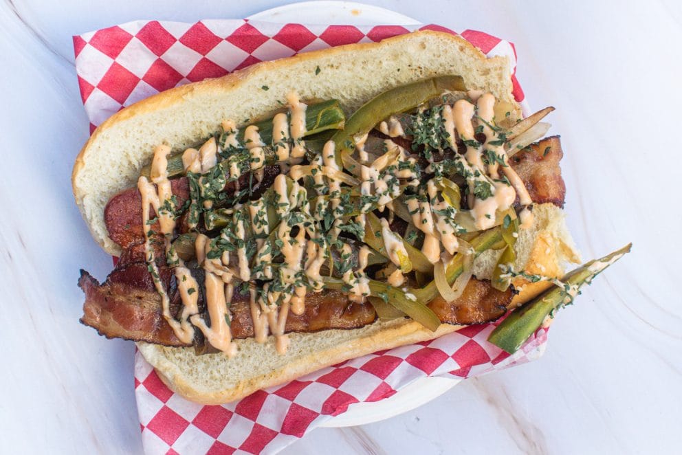 Bacon-wrapped dog topped with peppers and sauce